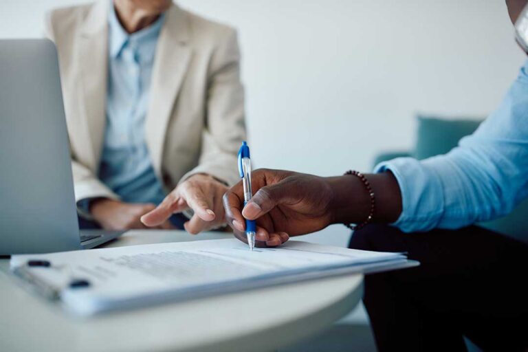Family members review a life insurance policy and funeral planning documents at a kitchen table.